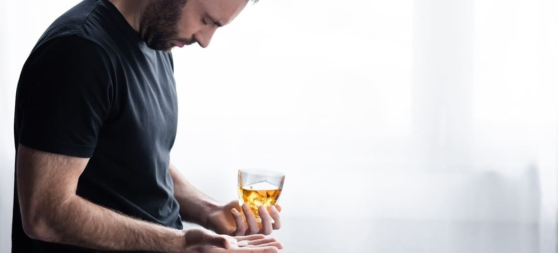 Мужчина держит в руках стакан со спиртным и таблетку