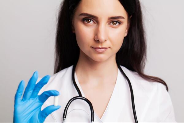 женщина врач держит в руке белую капсулу